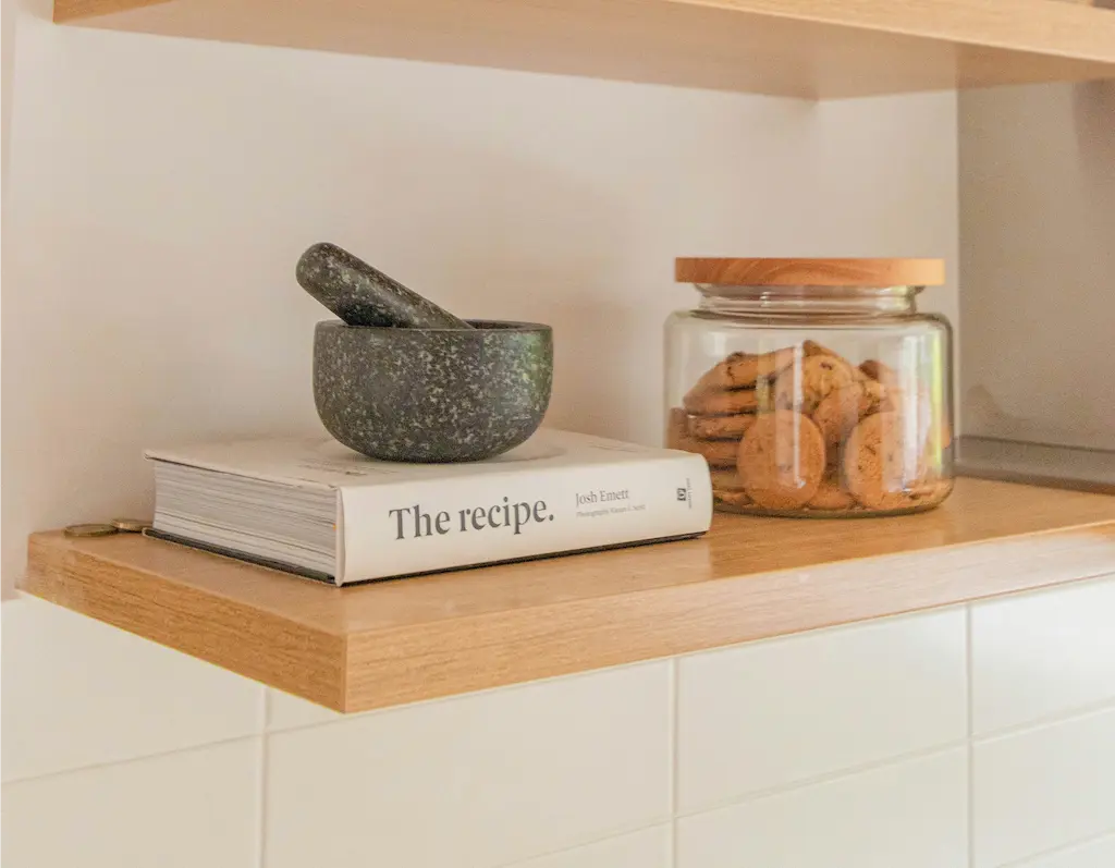 A shelf displaying a book alongside a bowl filled with freshly baked cookies, inviting and cozy atmosphere.